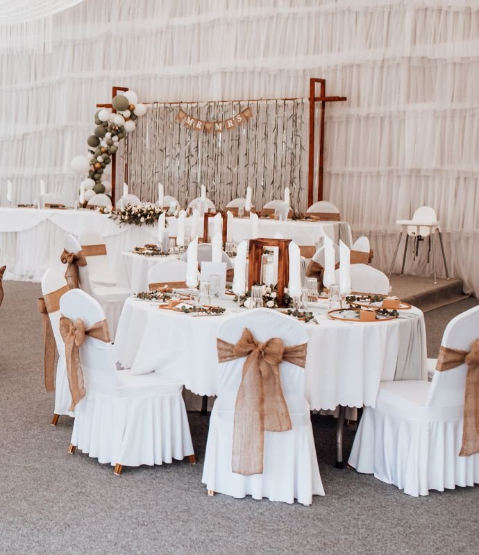 Ein Hochzeitsempfang in einem Zelt mit weißer Bettwäsche und Leinenschärpen.
