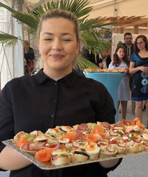 Eine Frau hält ein Tablett mit Essen vor eine Menschenmenge.