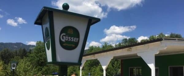 Schild im Laternenstil für Gösser-Bier vor dem Hintergrund eines klaren Himmels mit Bergen und einem Gebäude.