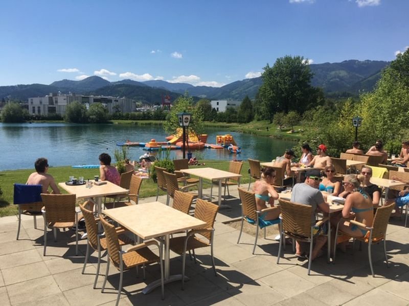 Eine Gruppe von Menschen sitzt an Tischen an einem See.